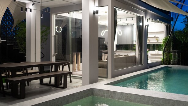 Un área de piscina moderna al aire libre, con zona de comedor y puertas de cristal que dan a un espacio habitable.