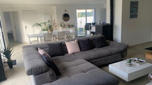 A modern living room with a grey sectional sofa, a white coffee table, and a dining area with a white table and chairs. - VILLA GRAVELOUP family vacation home, close to the sea and beaches (Erquy)