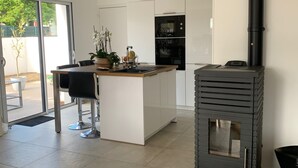 A modern kitchen with a central island, a built-in oven, and a wood-burning stove. - VILLA GRAVELOUP family vacation home, close to the sea and beaches (Erquy)