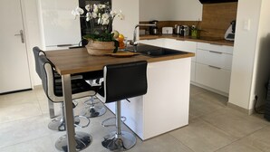 A modern kitchen with a wooden island, white cabinets, and a built-in oven. There are bar stools and a vase of white flowers on the island. - VILLA GRAVELOUP family vacation home, close to the sea and beaches (Erquy)