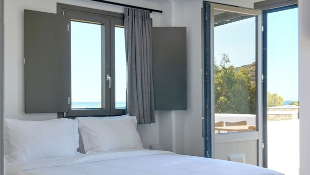 A bedroom with a bed, a window with curtains, and a view of the outdoors. - Emerald Tinos (Tinos)