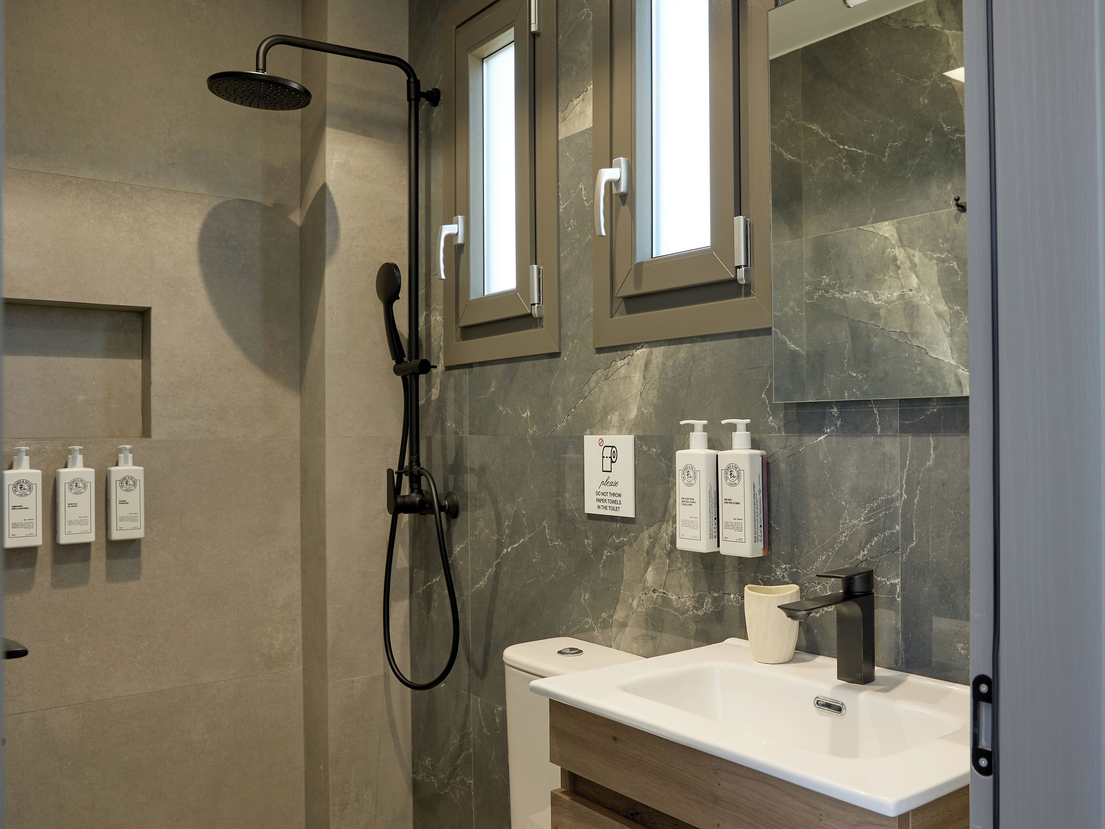 A modern bathroom with a shower, sink, and vanity. There are three bottles of shampoo and conditioner on the wall.