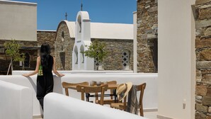 A terrace with white walls, stone accents, and a wooden table with chairs. - Emerald Tinos (Tinos)