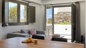 A modern living room with a sofa, a wooden table with lemons and a QR code, and a view of a stone building through open doors. - Emerald Tinos (Tinos)