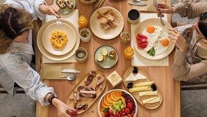 A wooden table with various dishes and food items, including fruits, vegetables, and meats, arranged for a meal. - Emerald Tinos (Tinos)