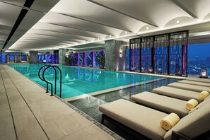 Una piscina interior moderna con sillas de descanso y vistas a la ciudad.