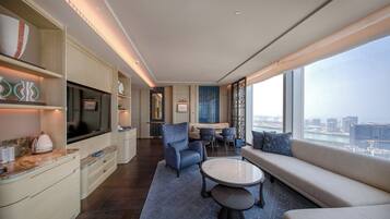 A modern hotel room with a large window, a sofa, a coffee table, and a dining area with chairs.