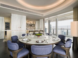 Un espace de salle à manger moderne avec une table ronde, des chaises recouvertes d’un tissu bleu et une vue sur la ville à travers de grandes fenêtres.