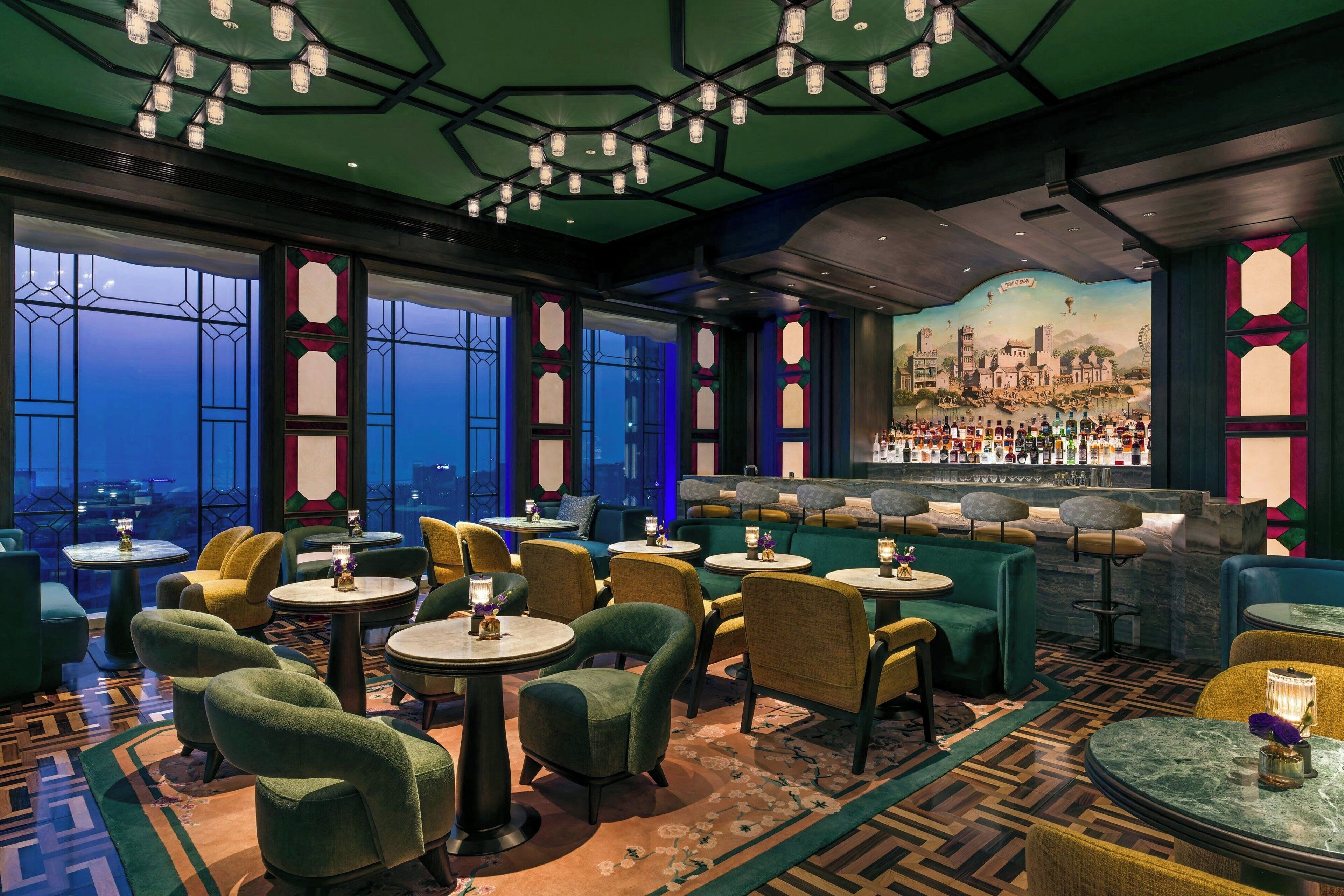 A bar area with round tables and chairs, large windows with decorative glass, and a mural of a cityscape on the wall.