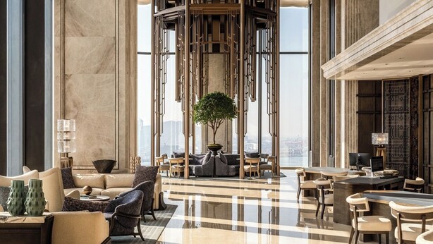Een ruime lobby met een centraal zitgedeelte, een decoratieve houten constructie en een groot raam met uitzicht op de stad.