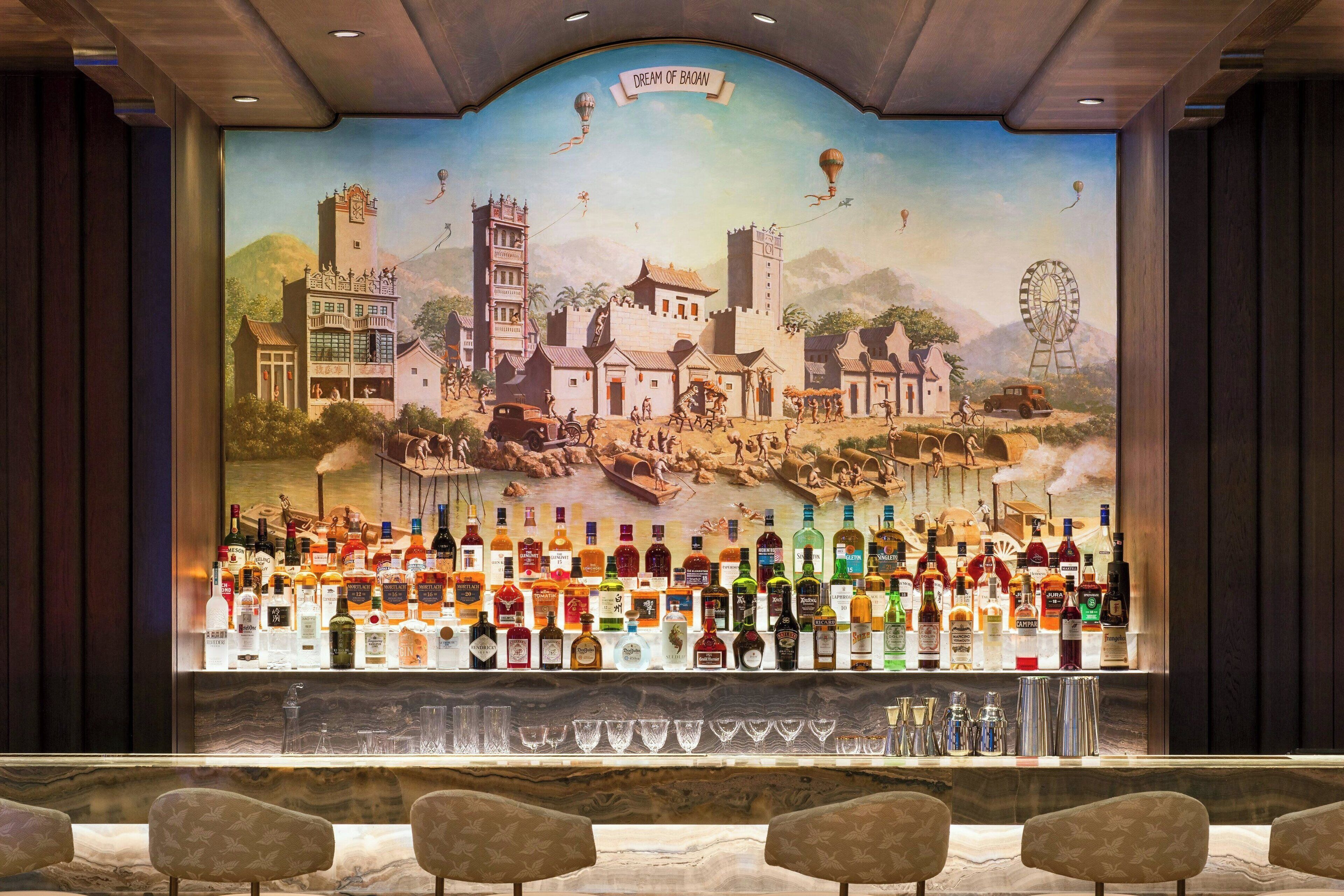 A bar area with a mural of a traditional town scene and a variety of liquor bottles.