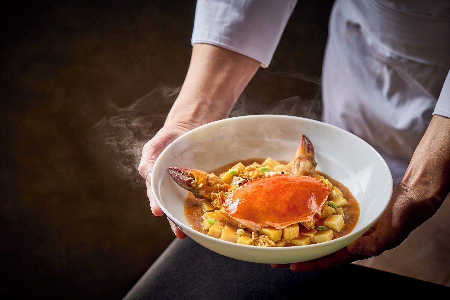 Uma pessoa segurando uma tigela de sopa de caranguejo com um caranguejo fumegante por cima.