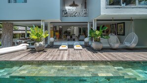 Una casa moderna con piscina, mobiliario exterior y sillas colgantes.