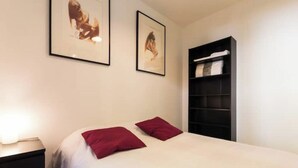 A bedroom with a bed, two pillows, a nightstand, a bookshelf, and two framed pictures on the wall. - T3 in green Grenoble city center (Grenoble)