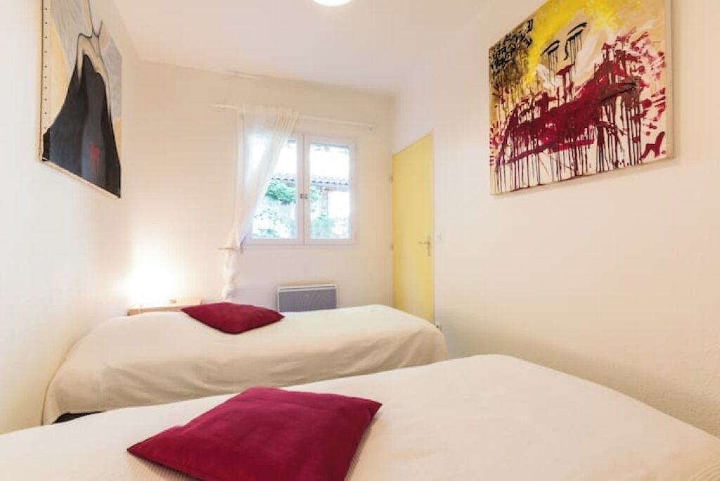 A hotel room with two beds, a window with curtains, a radiator, and a painting on the wall.