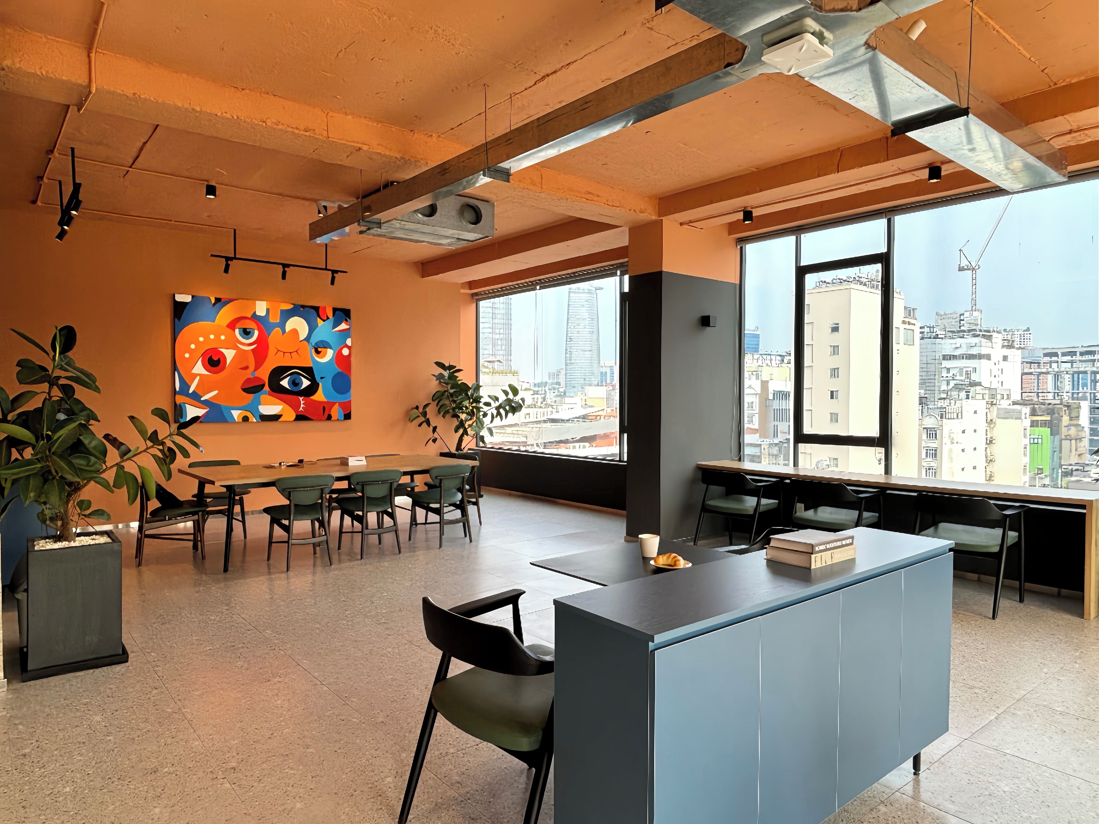 Un espace de bureau moderne doté d’une grande fenêtre donnant sur la ville, d’une table de réunion et d’une peinture abstraite aux couleurs vives accrochée au mur.