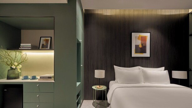 A modern hotel room with a bed, bedside lamps, a small table, a desk with a lamp, and a picture on the wall. - M Village Hotel Lý Tự Trọng, a brand of Modern Village Lifestyle (Ho Chi Minh City)