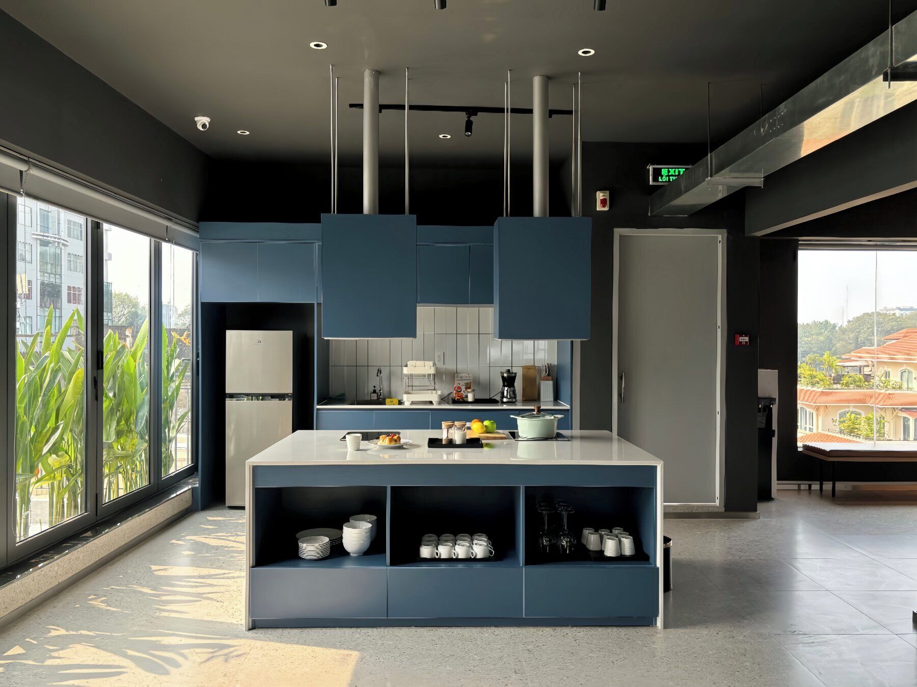 A modern kitchen with a central island, built-in shelves, and a view of the city through large windows.