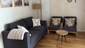 A modern living room with a dark grey sofa, two armchairs, a round wooden coffee table, and a woven pendant light. - Magnificent new 60m2 apartment in an exceptional location! (Samoëns)