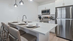 Une cuisine moderne dotée d’un îlot central, d’appareils électroménagers en acier inoxydable et de luminaires suspendus.