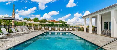 A swimming pool with lounge chairs and umbrellas, surrounded by a covered area with columns.