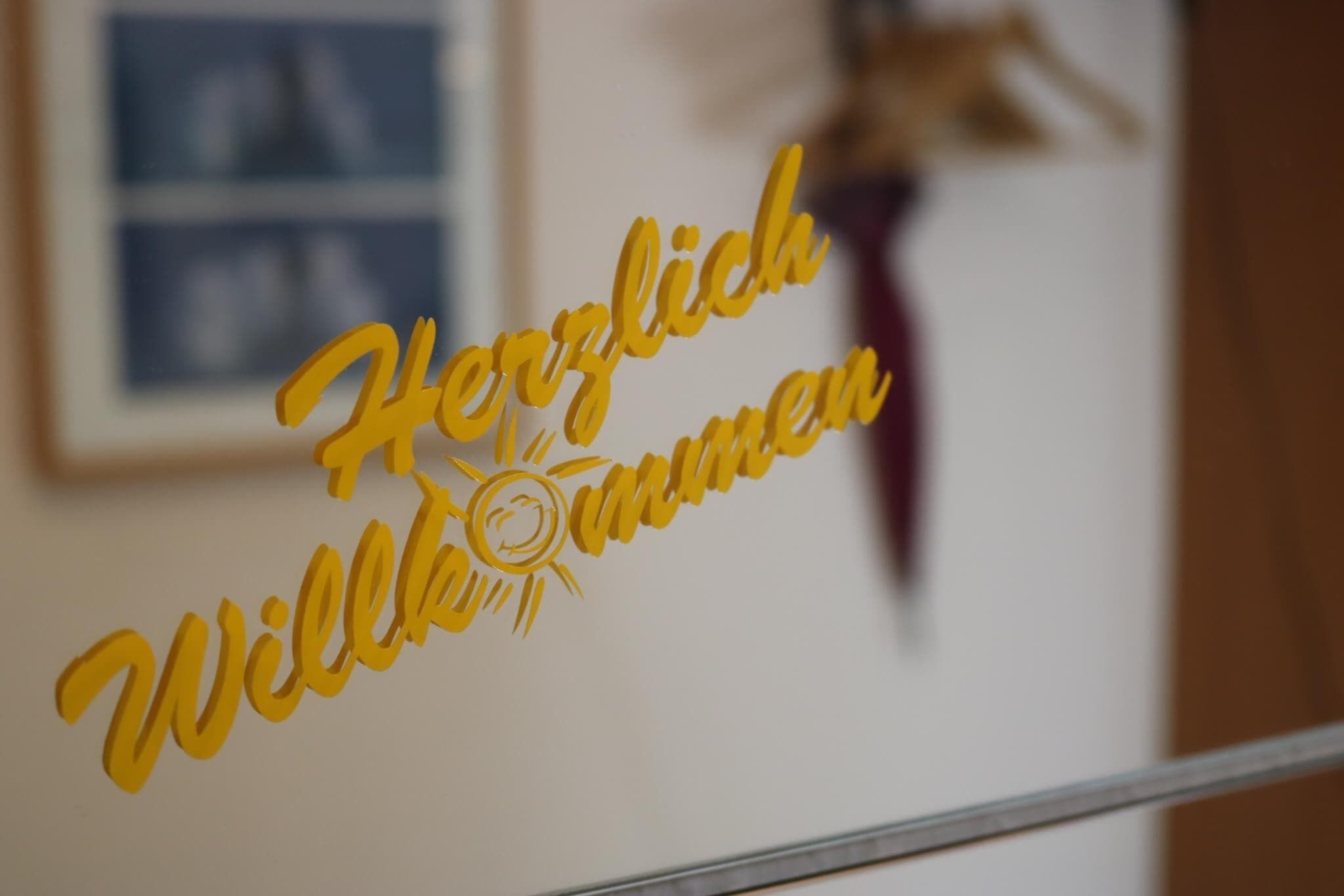 Eine Wand mit einem gelben Schild, das 'Herzlich Willkommen' und eine Sonne zeigt.