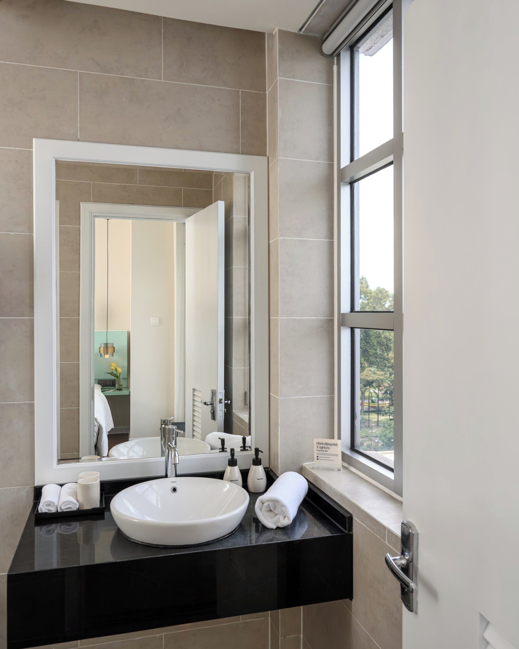 A modern bathroom with a large mirror, two sinks, and a window providing a view of the outdoors.