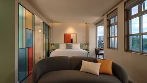 Una habitación de hotel moderna con una cama grande, un sofá y vistas de la ciudad a través de amplios ventanales.