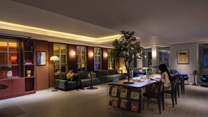 Una sala de estar moderna con un sofá, una mesa de centro y un comedor con sillas. Incluye una estantería y una planta en maceta.
