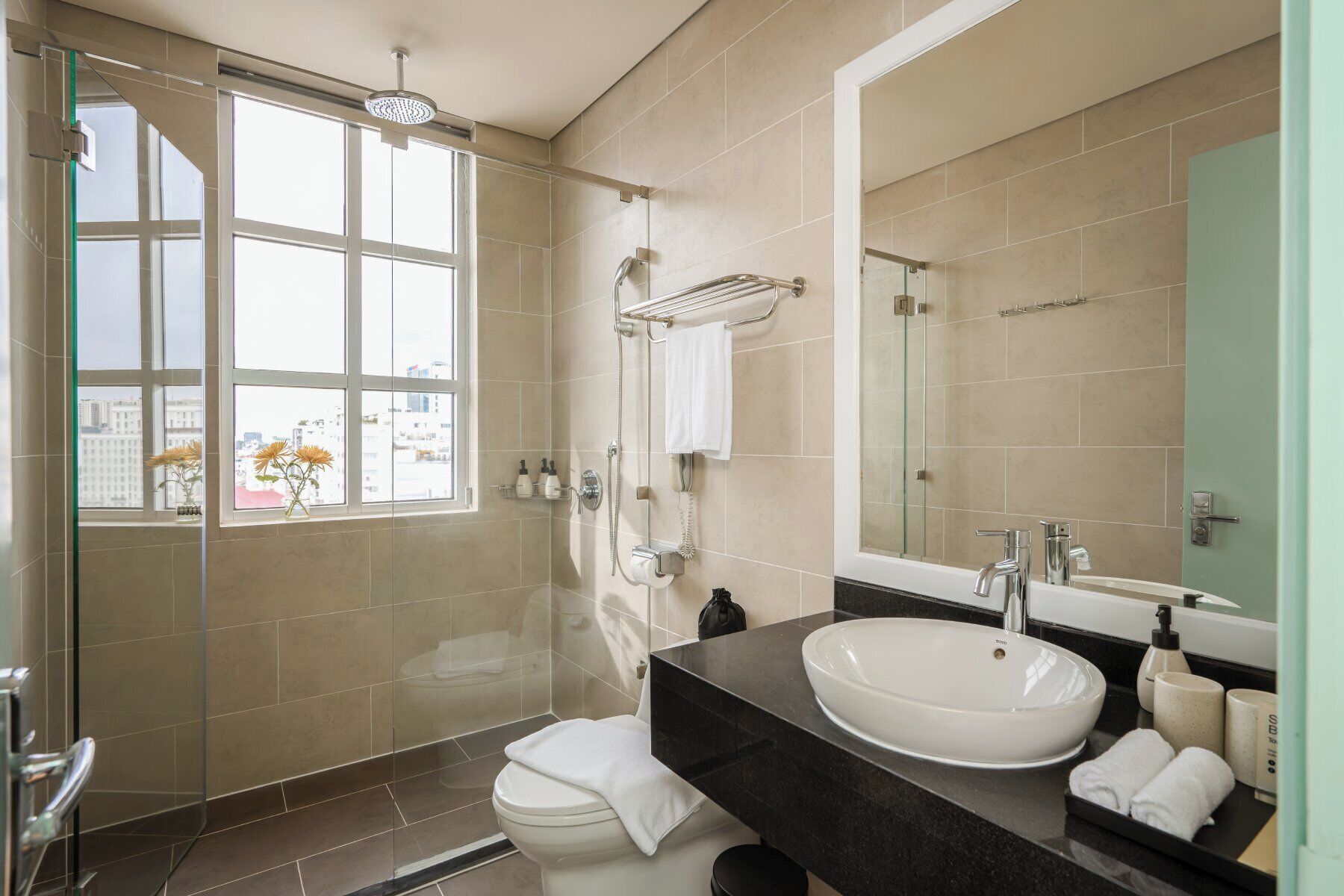 Un baño moderno con cabina de ducha de vidrio, un espejo grande, un lavabo con encimera negra y un inodoro.