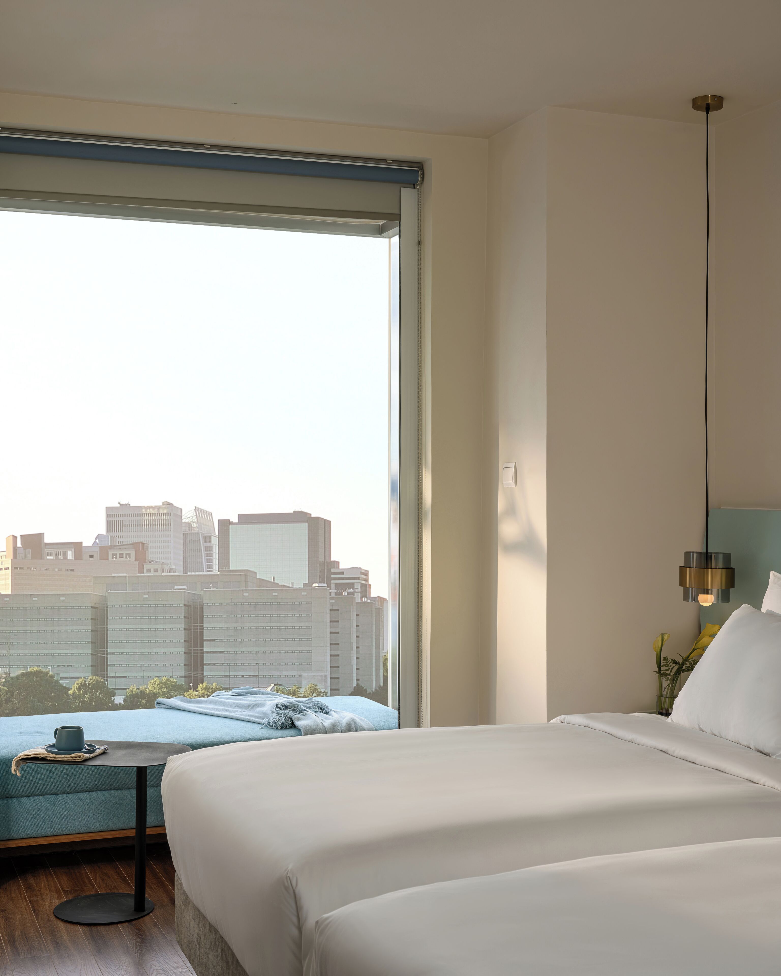 Un hotel moderno con una cama grande, un escritorio con silla y vistas a la ciudad a través de un ventanal amplio.