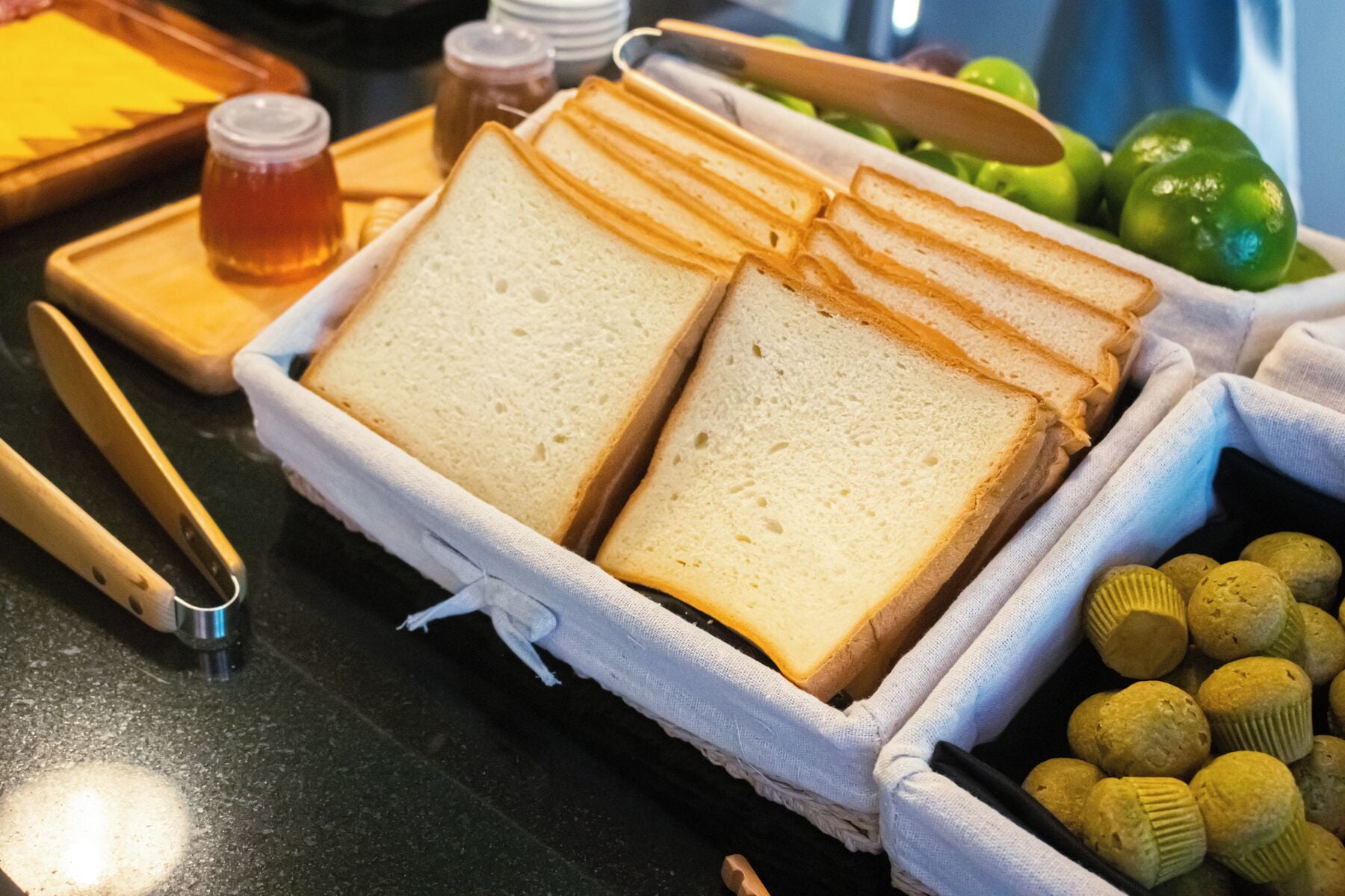 Ein Tablett mit Brotscheiben, ein Honigglas und einige Muffins auf einem Tisch.