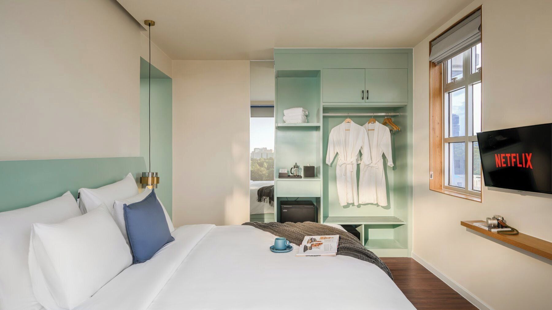 A hotel room with a bed, a wardrobe, a television, and a window with a view.