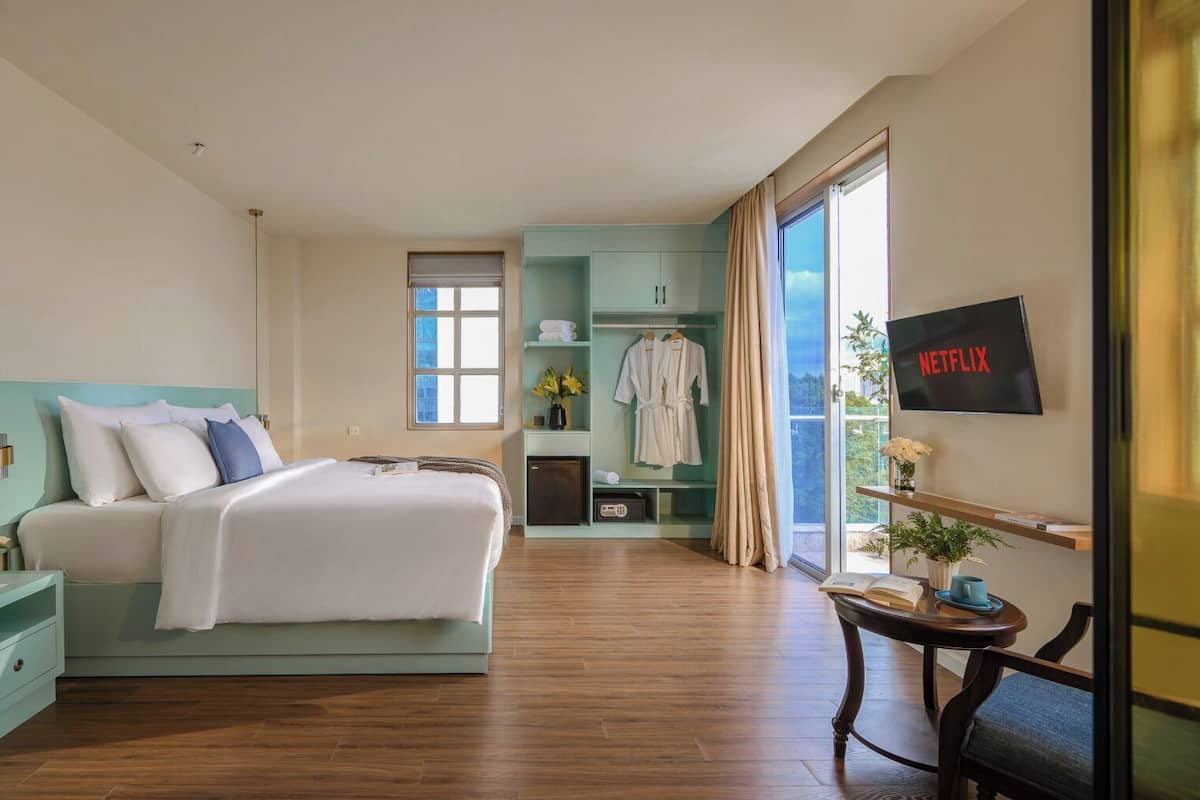 A hotel room with a bed, bedside tables, a TV, a desk, and a window with curtains.