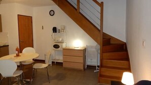Een eetgedeelte met een ronde tafel en stoelen, een houten trap en een klok aan de muur.
