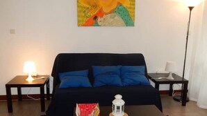 Een kamer met een bed, een tafeltje, een lamp en een schilderij aan de muur.