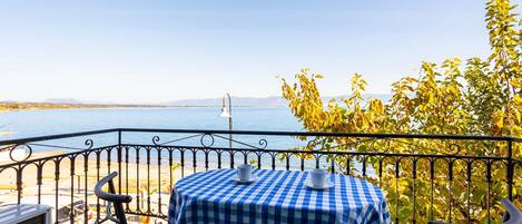 A balcony with a checkered tablecloth, two chairs, and a view of the sea.