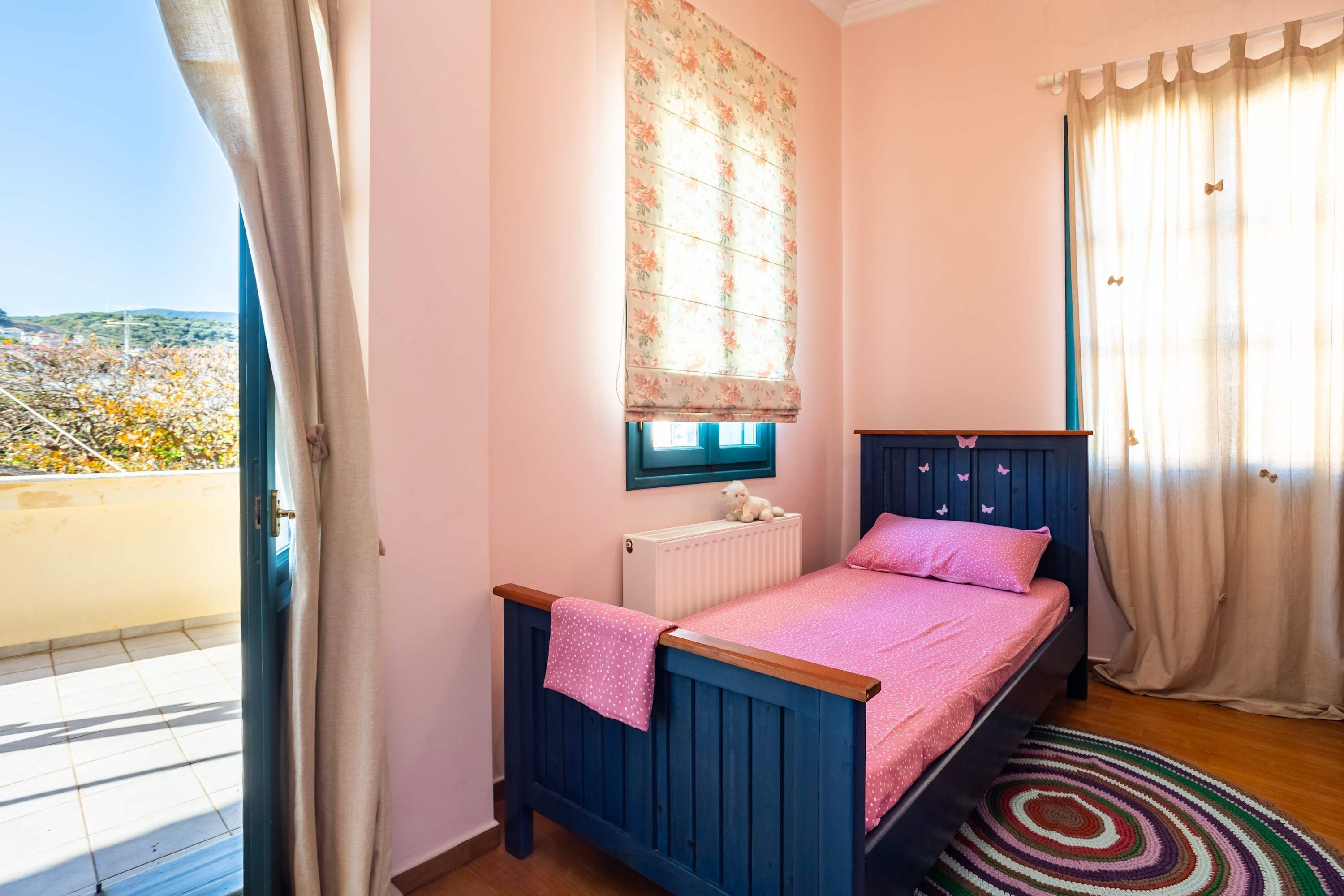 A bedroom with a bed, a window with curtains, a radiator, and a view of the outside.