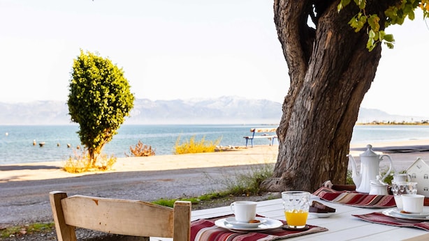 A table set with a white tablecloth, a wooden chair, and a view of the sea and mountains.