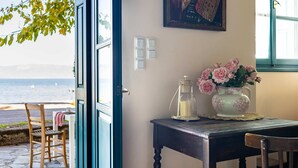 An open door leading to a room with a table, a vase of flowers, and a view of the sea.