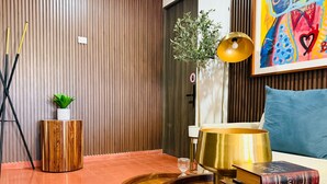 A room with a wooden floor, a round wooden table with books, a lamp, and a plant.