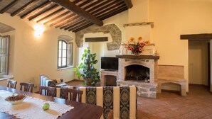 A cozy living room with a stone fireplace, wooden beams, a television, and a dining area with a table and chairs.
