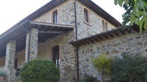 A stone building with a tiled roof, arched windows, and a covered porch area.