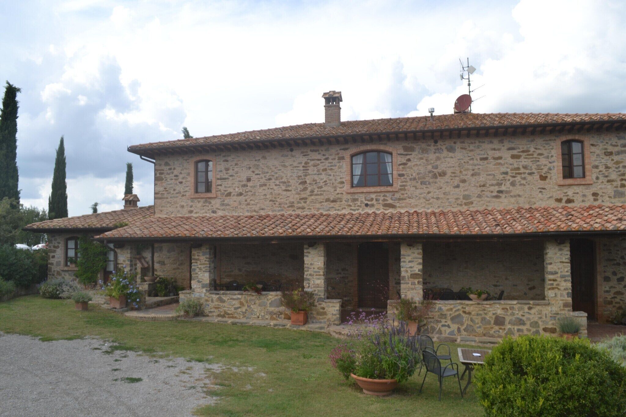 A stone house with a tiled roof, a covered porch, and potted plants.