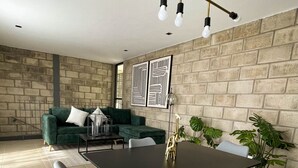 Un salon moderne avec un coin repas, comprenant un mur en pierre, un canapé vert et une table à manger avec des chaises.