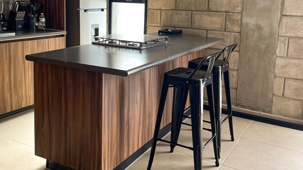 Une cuisine moderne dotée d’un îlot central, de tabourets de bar, d’un réfrigérateur en acier inoxydable et d’une horloge murale.