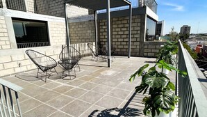 Une terrasse sur le toit, dotée d’un espace salon couvert, d’une plante en pot et offrant une vue sur le paysage urbain.