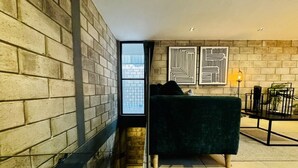 A modern living room with a brick wall, a green sofa, and two abstract art pieces.