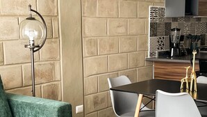 Una sala de estar moderna con un sofá verde, una mesa de comedor con sillas, un reloj de pared y una zona de cocina con cafetera.