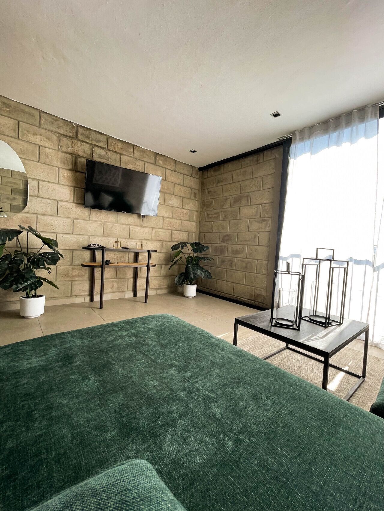 Ein modernes Wohnzimmer mit Backsteinwand, Flachbildfernseher, grünem Sofa und Topfpflanzen.